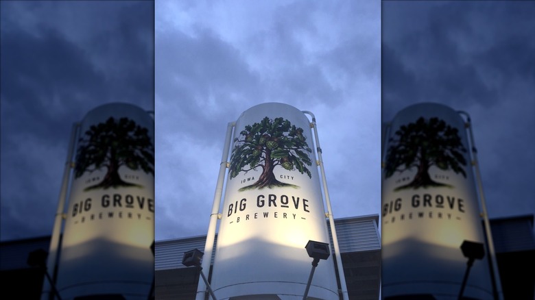 Tall white lit industrial silo outside of Big Grove Brewery with a tree logo on and the words "Iowa City" and "Big Grove Brewery" on it at night