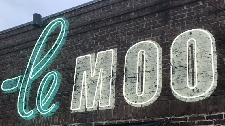 Exterior of Le Moo restaurant; weathered dark brick wall with a neon letters reading "Le" in blue and "Moo" in white
