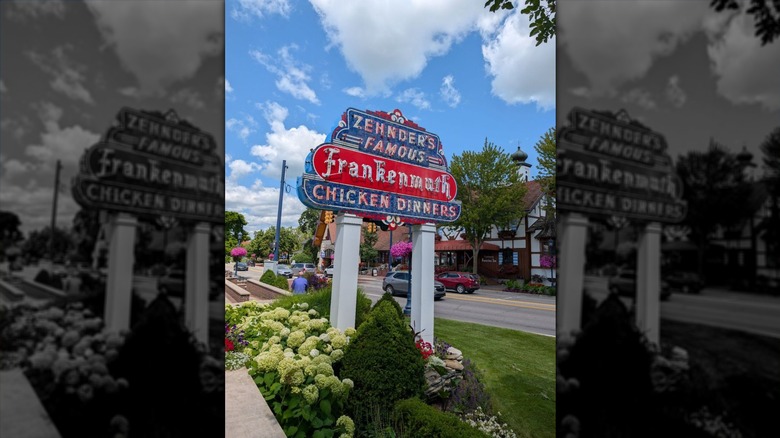 A red, white, and blue vintage outdoor sign set in a flowerbed that reads, "Zehnder's Famous Frankenmuth Chicken Dinners"