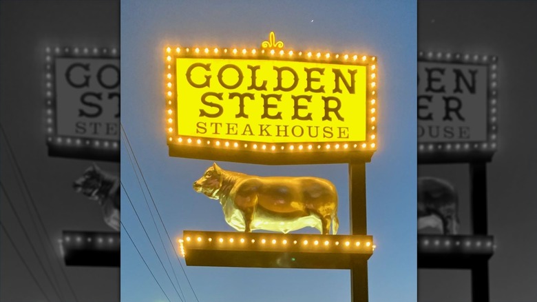A yellow vintage outdoor sign, lit at night, that reads "Golden Steer Steakhouse" in brown with a gold steer sculpture below it