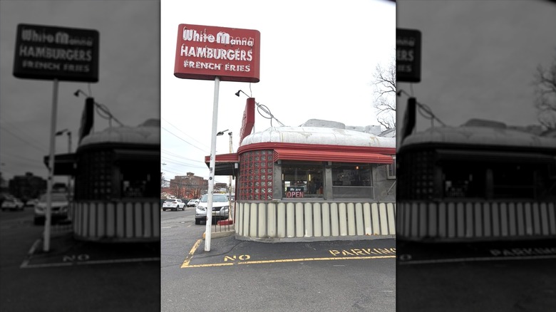 The exterior of White Manna during the day, showing the red neon sign with "White Manna Hamburgers French Fries" in white; white and red metal single-story building with windows appears on the right