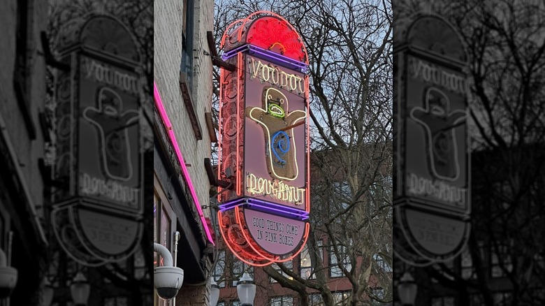 The outdoor neon sign for Voodoo Doughnut at dusk depicting a ghost with red, purple, blue yellow and green neon colors