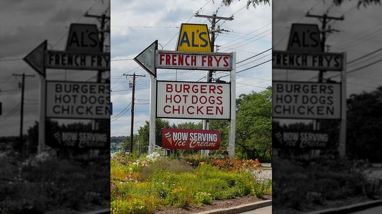 The exterior sign for Al's French Frys: "Al's" written on top in blue against a yellow background; "French Frys" is in a white arrow facing left in red letters; "Burgers, hot dogs, chicken" written in red on a white background below it; and "Now serving Ice Cream" is in white on a maroon background below it