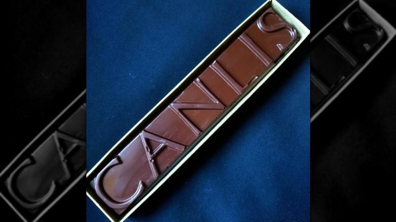 An oblong box set diagnolly on a blue tablecloth; a chocolate bar with "Canlis" embossed on it is in the box