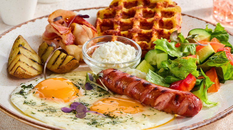 Traditional breakfast patter with waffle, sausage, potatoes, bacon, egg and side salad