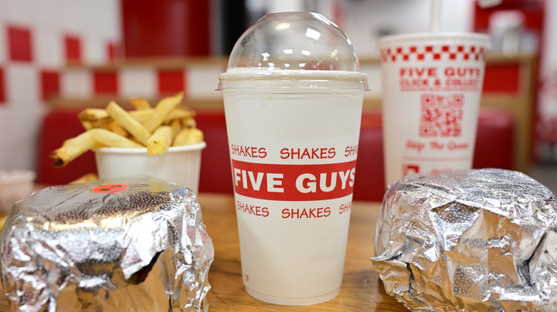 Five guys meal of two burgers, fries, a shake, and a soda on a table inside a restaurant