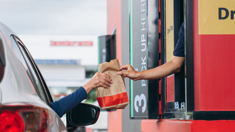 person grabbing bag from cashier at drive thru