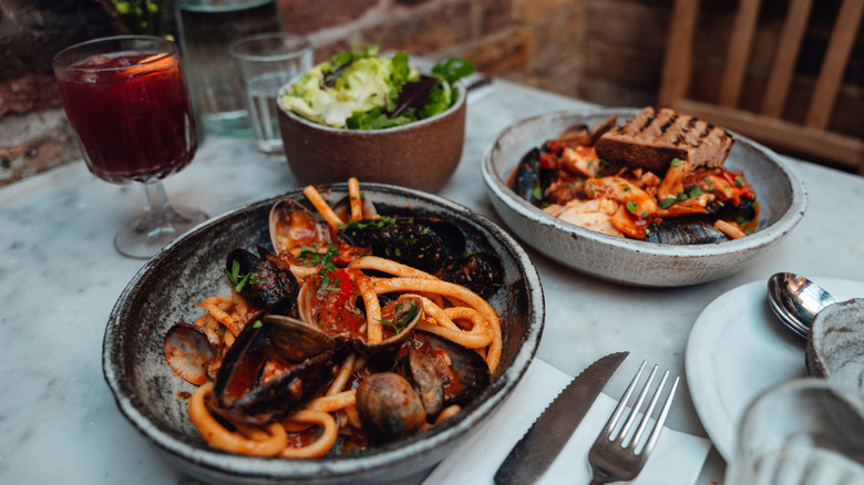 Two Italian meals on a table outside a restaurant. A small salad and a cocktail is visible.