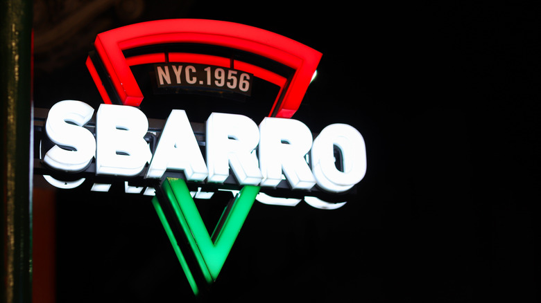 Neon signage for Sbarro pizza; shown at night.
