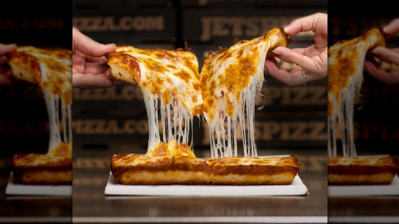 two people picking up cheesy jets pizza slice