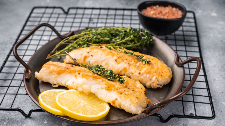 Two cod fillets sitting on a plate with a side of lemon.