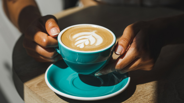 A person holds a hot latte in a blue mug