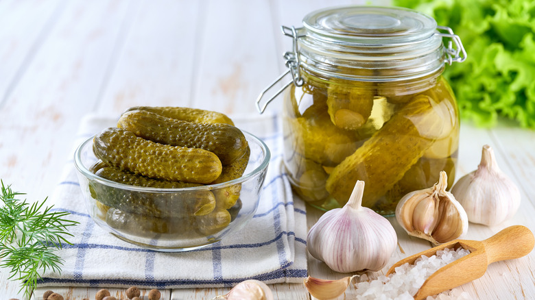Pickles in a bowl next to pickles in a jar with various ingredients around them