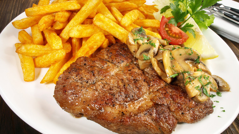 Pork shoulder steak on plate with fries and mushrooms