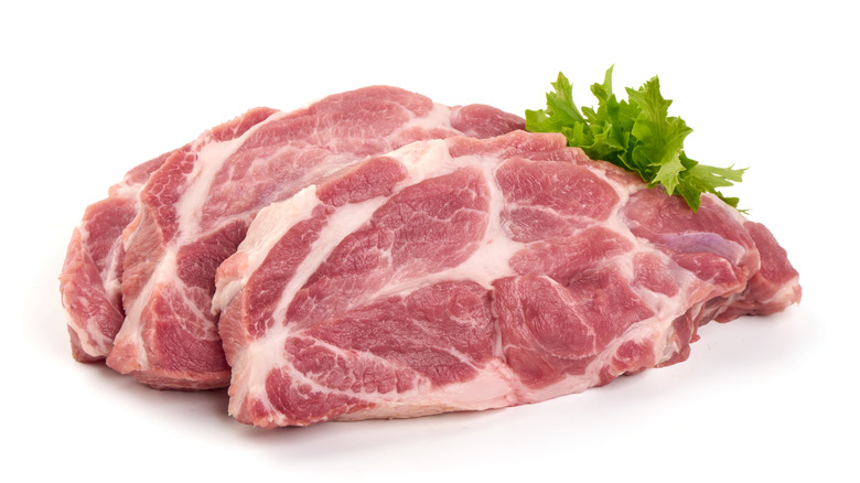 Sliced, raw pork shoulder steaks with lettuce