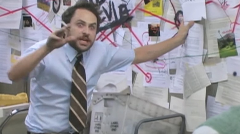 Charlie Kelley gestures wildly before a board covered with documents connected, conspiracy-style, with threads.