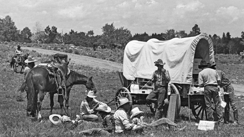 Cowboys gathered around a chuckwagon during a cattle drive.