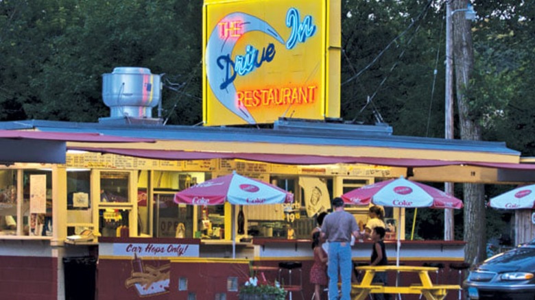 Neon Sign of The Drive In Restaurant and exterior with red and white umbrellas and picnic tables