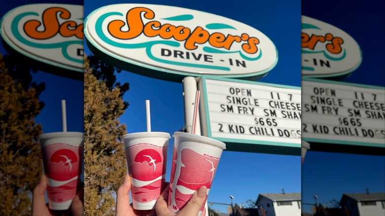 Two styrofoam drink cups held in front of scoopers drive in sign