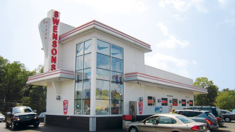 Exterior of Swensons Drive-In Restaurant and parking lot with cars and sign