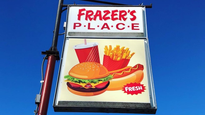 Frazer's Place sign featuring burgers shake hot dog and fries in front of blue sky.