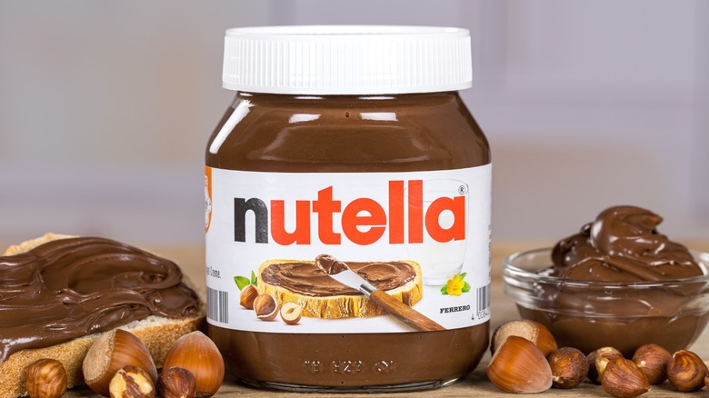 A jar of Nutella, flanked by Nutella in a bowl and spread on bread.