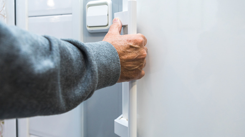A hand grabbing a fridge door handle