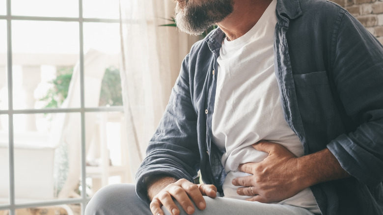 A person holding their stomach while sitting near a window