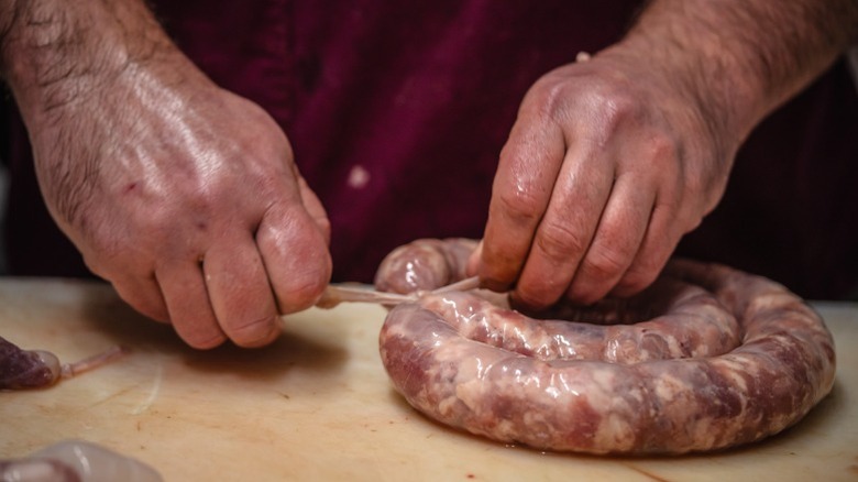 A man closing up a sausage casing.