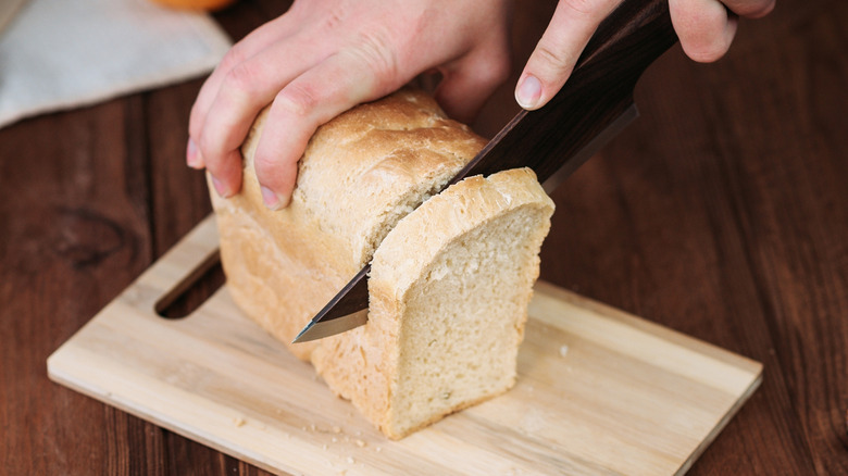 A loaf of bread being sliced for a sandwich