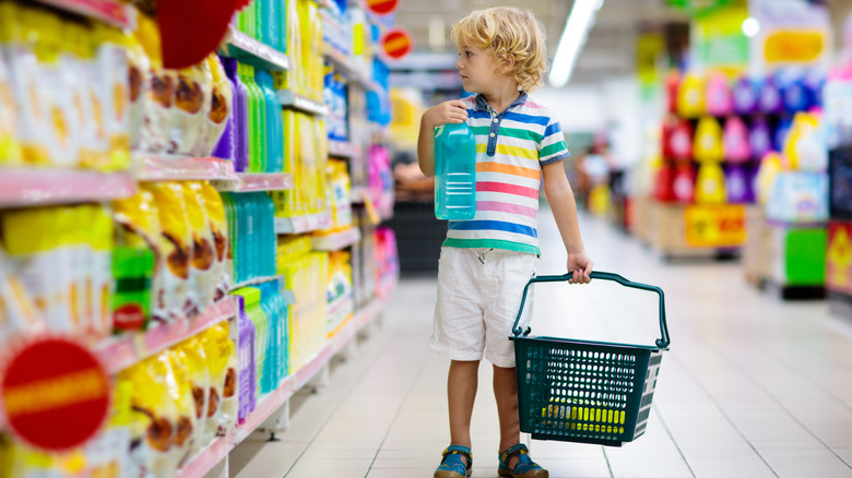 Child carrying grocery basket and looking at colorful juice bottles on shelf