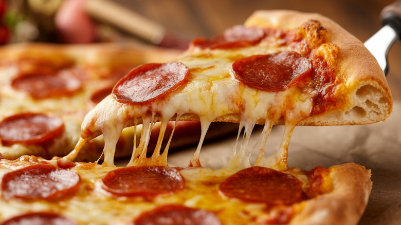 A slice of pepperoni pizza with extra cheese being picked up by a pie server