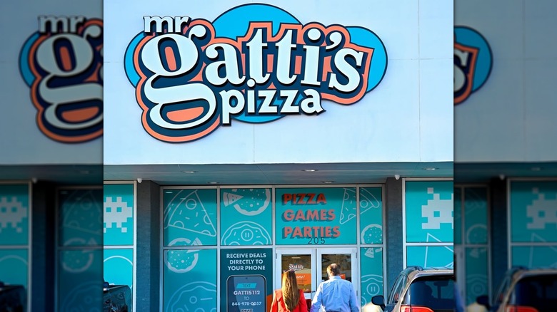 Two people walking into a standalone Mr. Gatti's Pizza during the daytime