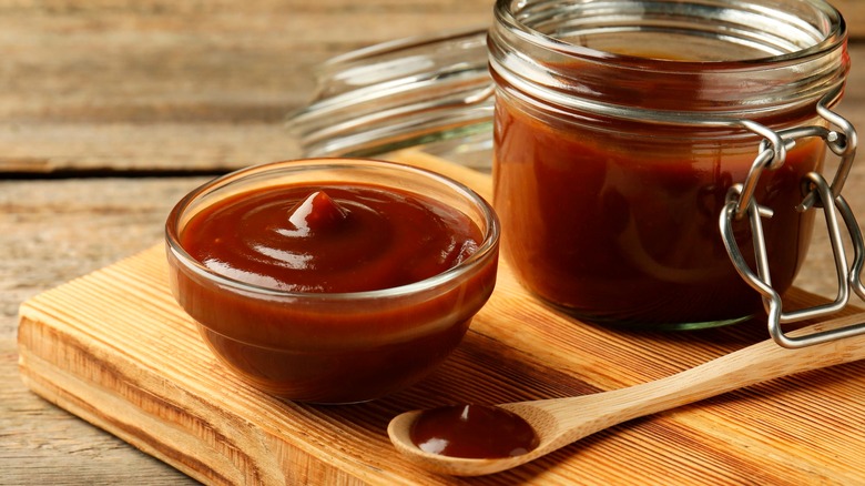 BBQ sauce in a jar and in a glass bowl on a wooden board