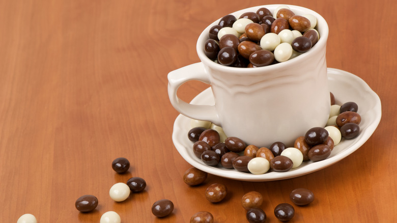 Brown and white chocolate-covered espresso beans in a white coffee mug