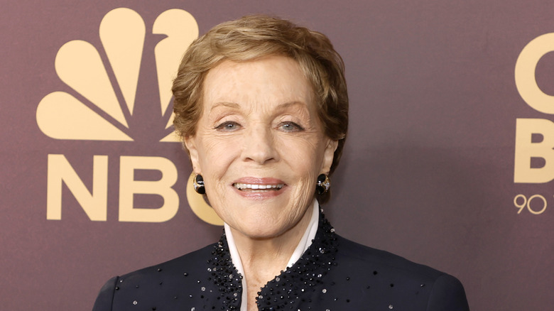 Julie Andrews headshot on red carpet wearing black jacket behind NBC logo