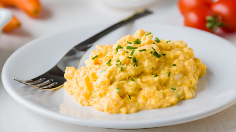 hands holding a plate of scrambled eggs with chopped chives