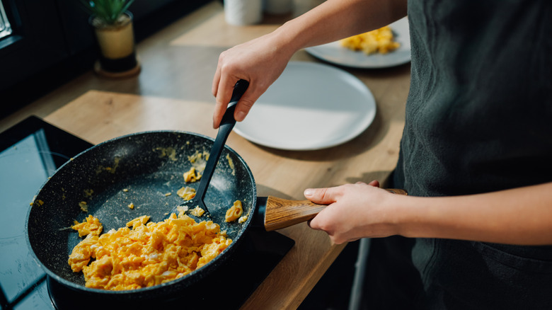 person scrambling eggs in a black frying pan