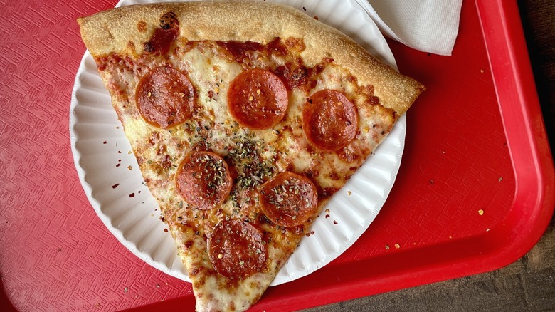 A New York-style pizza slice on a paper plate and a red tray.