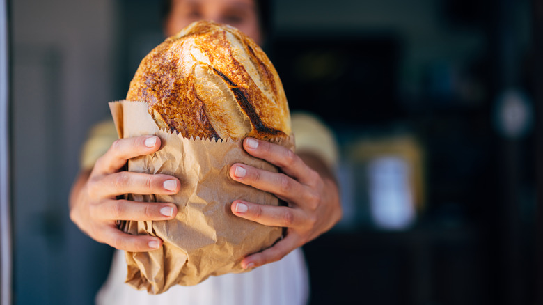A baker holding out a loaf of bread in brown paper.