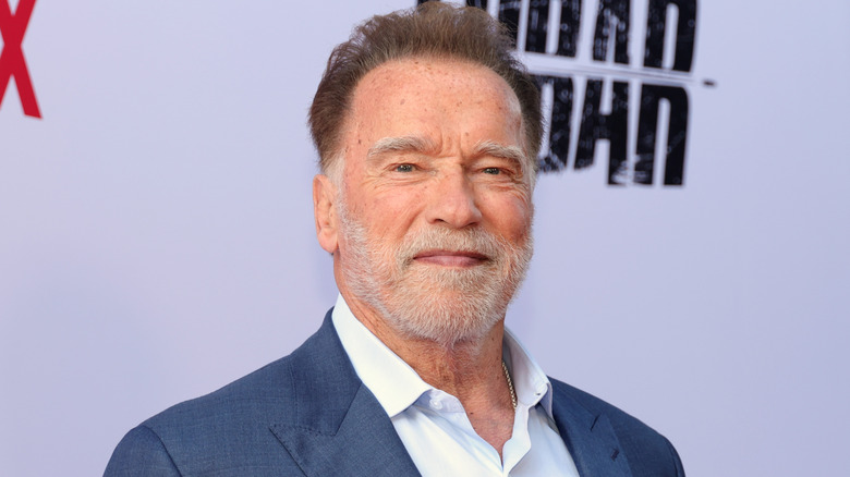 Arnold Schwarzenegger wearing a blue suit and white shirt and smiling at the camera