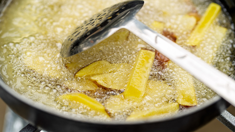 French fries cooking in a pan of hot oil with slotted spoon