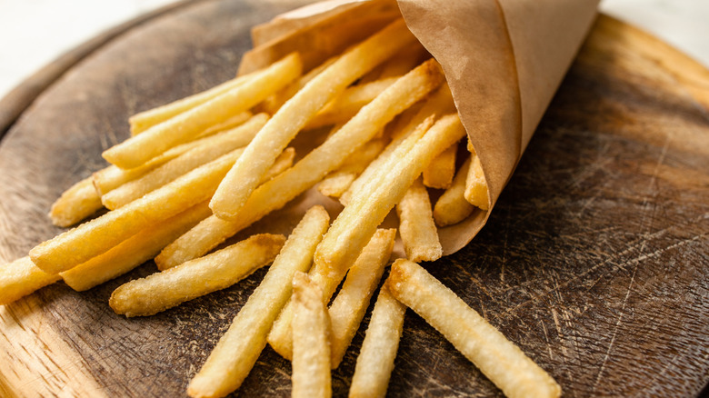 Cooked French fries spilling out of a brown paper bag onto wood surface