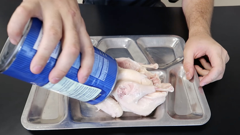hands pouring whole chicken from can into metal tray