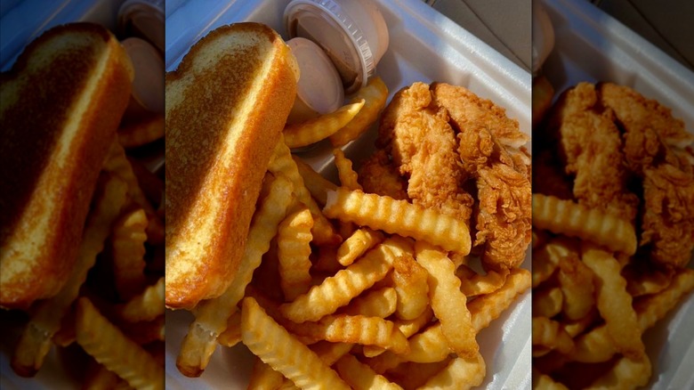 A takeout container with toasted bread, chicken fingers, crinkle fries, and two small containers of signature sauce from Guthrie's