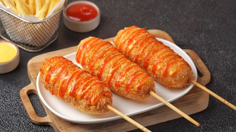 Three corn dogs on a plate, drizzled with ketchup.