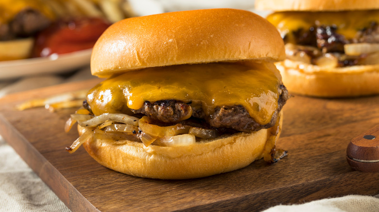 An Oklahoma Onion Burger with fried onion strings and cheese on a wooden board