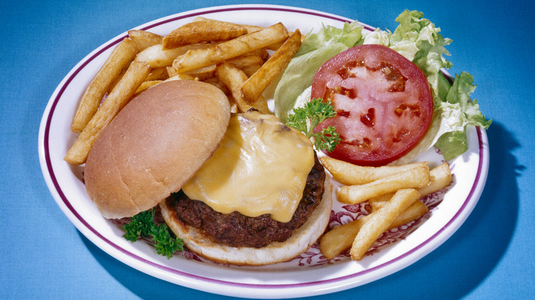 A cheeseburger on a white plate with fries, lettuce, and tomato