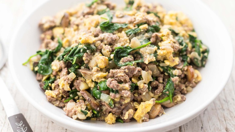 A plate of Joe's Special with spinach, ground beef, and mushrooms in a bowl.
