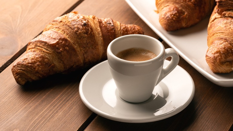 A cup of Neapolitan espresso on a saucer next to several croissants.